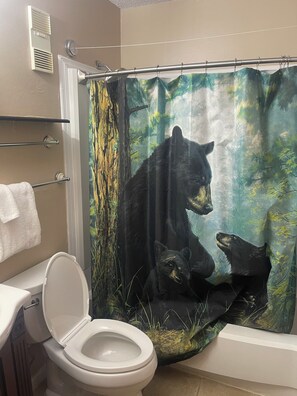 Un baño con inodoro, cortina de ducha con motivo de bosque y un perchero.