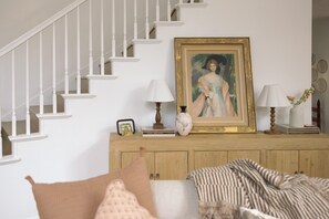 Eine Treppe mit weißen Balustern, ein Holzkonsolentisch mit einem gerahmten Gemälde, zwei Lampen und eine Vase mit Blumen.