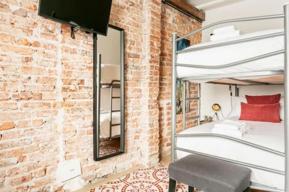 A room with a brick wall, a bunk bed, a flat-screen TV, and a mirror.