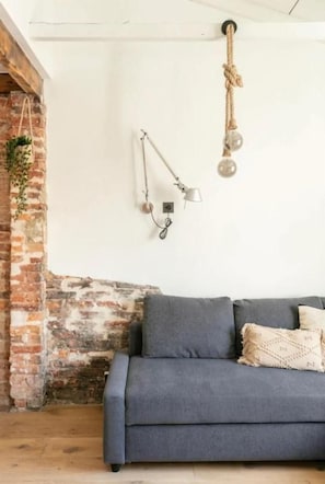 A room with a blue sofa, a hanging light fixture, and a brick wall. - Good Vibe Rooms (Bilbao)