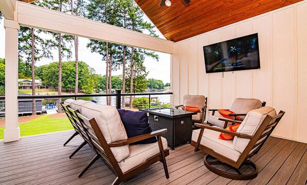 A covered outdoor seating area with wicker furniture and a flat-screen TV mounted on the wall.