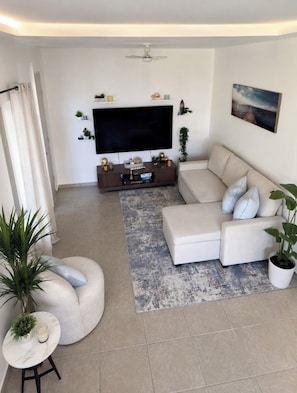 Un saló modern amb un sofà modular, una televisió de pantalla plana, un ventilador de sostre i un quadre a la paret.