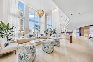 Een ruime hotellobby met een modern design, met een grote zithoek met sofa’s en fauteuils, een centrale salontafel en potplanten.