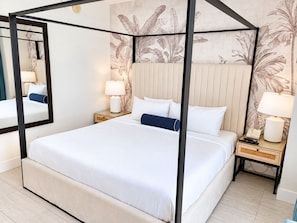 Een bed met hemelbed, twee nachtkastjes met lampen, en een muur met een tropisch bladmotief.