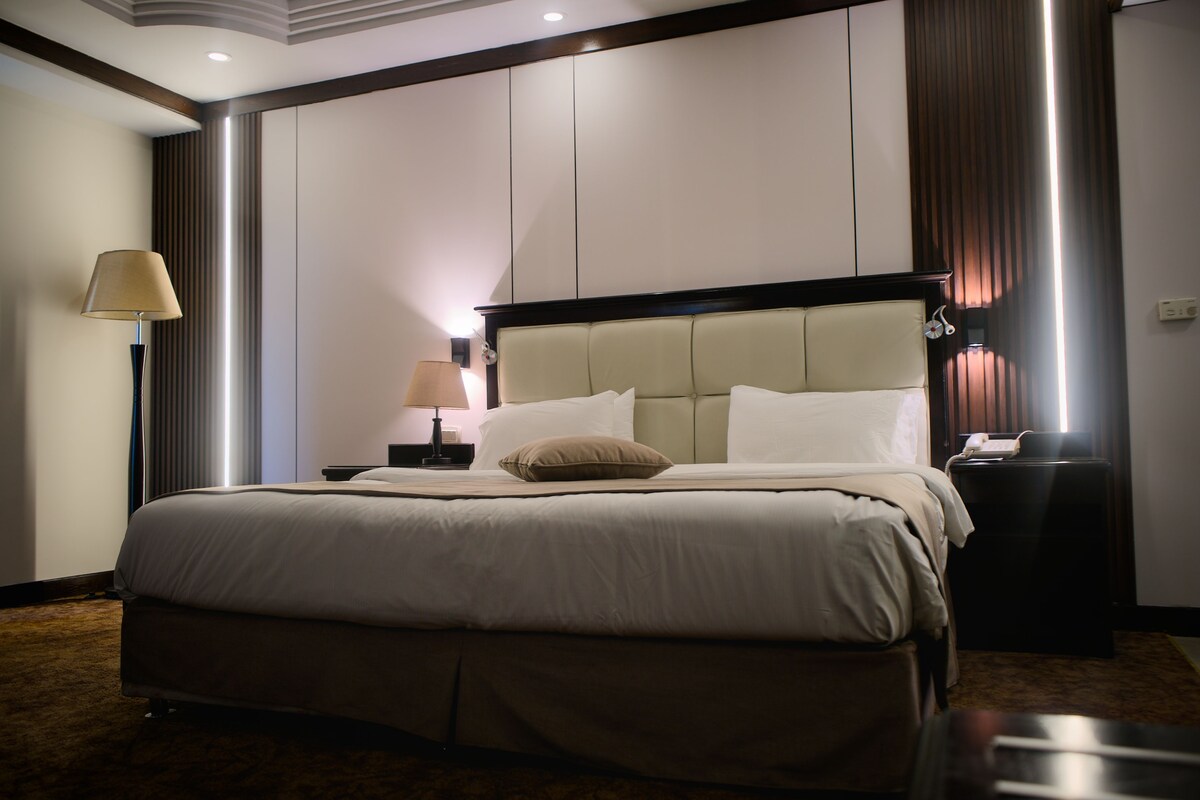 A hotel room with a large bed, a bedside table with a lamp, and a telephone.
