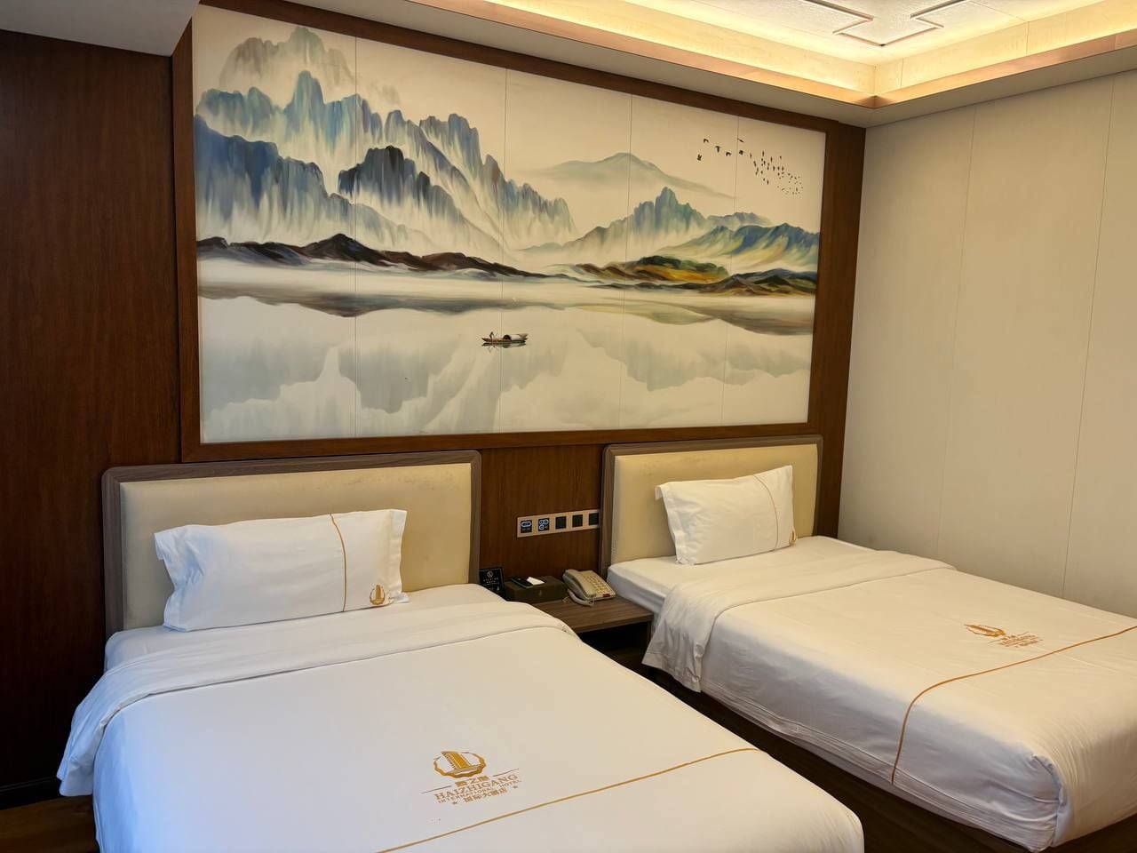 A hotel room with two beds, a large wall mural, and a wooden headboard.