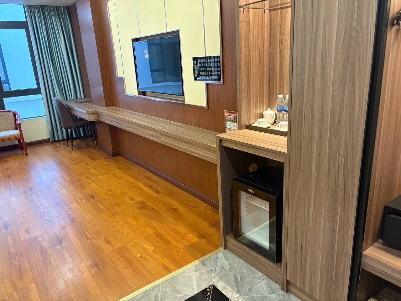 Une chambre d’hôtel avec un plancher en bois, un four à micro-ondes encastré, un petit four et un téléviseur fixé au mur.
