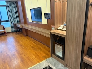 Una habitación de hotel con piso de madera, microondas integrado, horno pequeño y televisor montado en la pared.