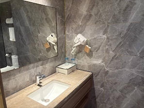 Un baño con lavamanos de mármol, espejo, secador de pelo y toallero.