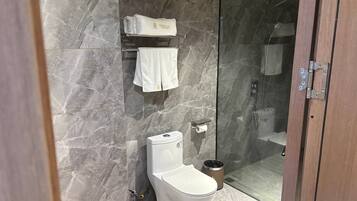 Une salle de bain moderne avec un mur en marbre, des toilettes, une douche en verre et un porte-serviettes avec des serviettes pliées.