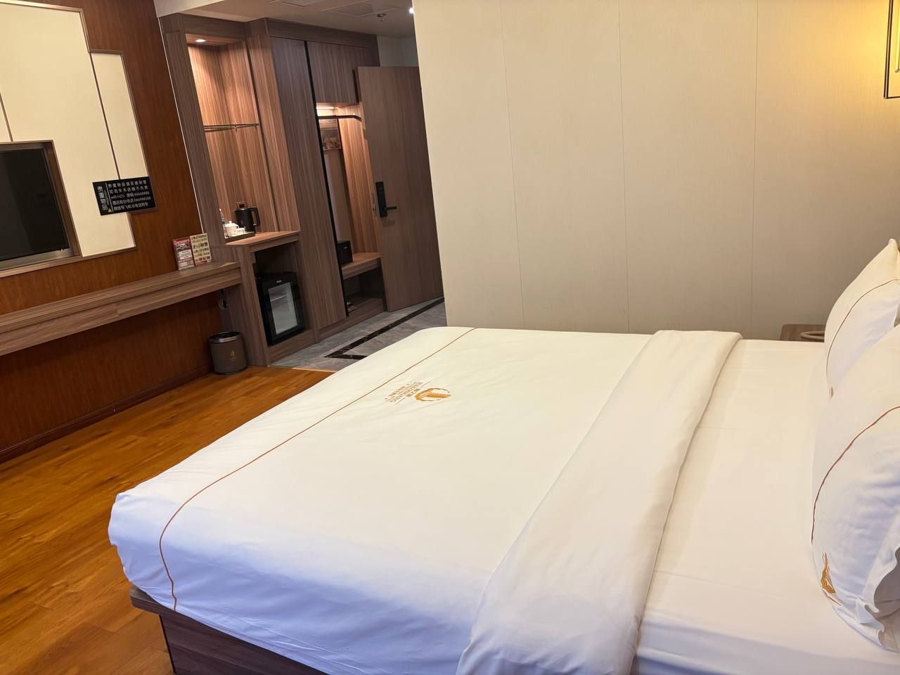 Une chambre d’hôtel avec un lit, un plancher en bois, un bureau avec un ordinateur et un miroir.