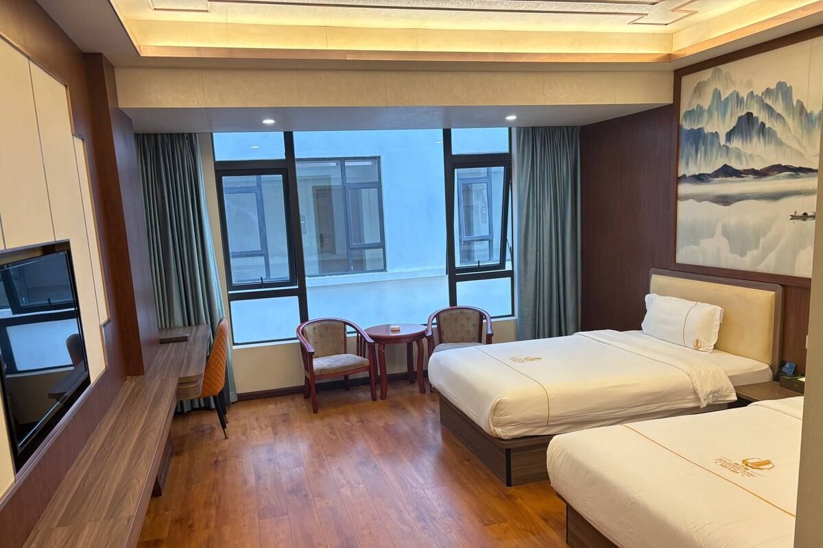 A hotel room with two beds, a desk, a chair, and a television.