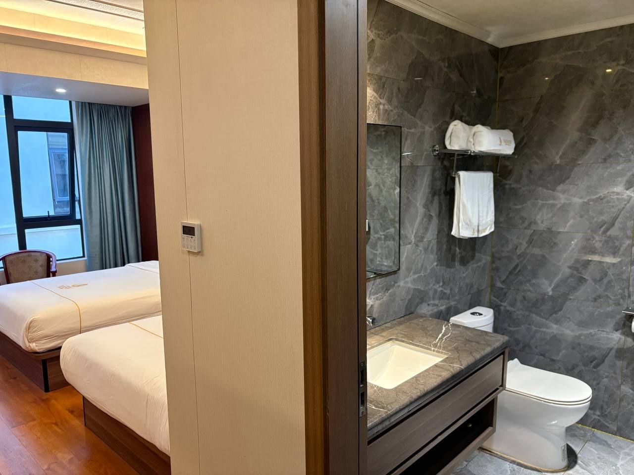 A hotel room with a bed, a bathroom with a marble sink and a toilet, and a window with curtains.