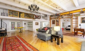 A spacious living area with a high ceiling, a chandelier, a sofa, a coffee table, and a dining area with chairs and a table. - TIMELESS ROME APARTMENT WITH PARQUET FLOORS AND A FULLY EQUIPPED KITCHEN (Roma)