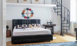 A bedroom with a large bed, a circular wall decoration, a sewing machine, and a spiral staircase. - TIMELESS ROME APARTMENT WITH PARQUET FLOORS AND A FULLY EQUIPPED KITCHEN (Roma)