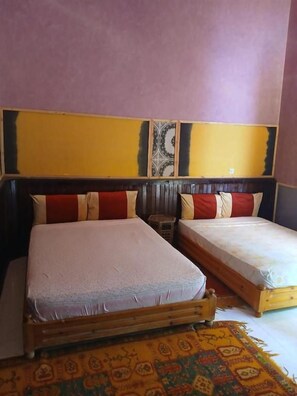 A room with two beds, a patterned rug, and a plain wall with a decorative panel. - Chez moulay ismail (Tamnougalt)