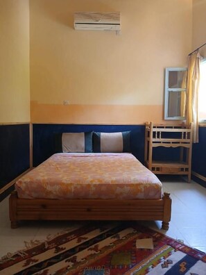 A bedroom with a bed, a window, an air conditioning unit, and a wooden bench. - Chez moulay ismail (Tamnougalt)