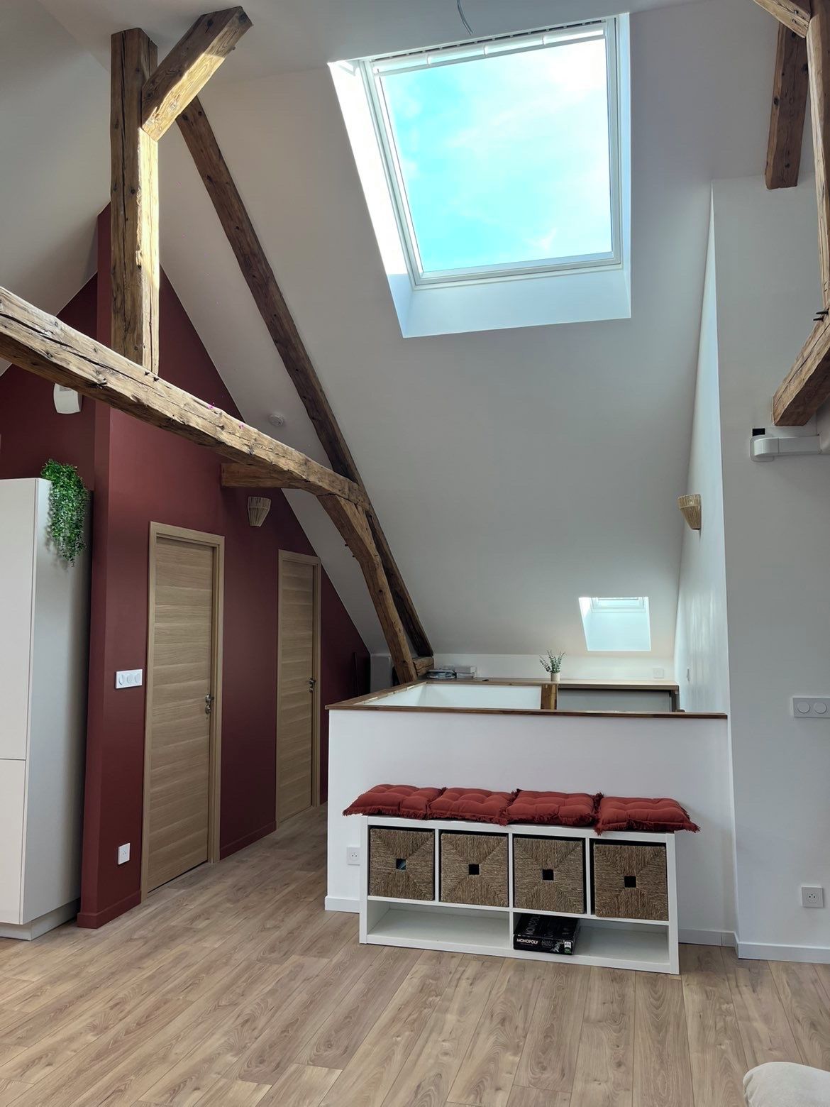 A loft bedroom with a skylight, wooden beams, a white wardrobe, and a built-in bench with storage.