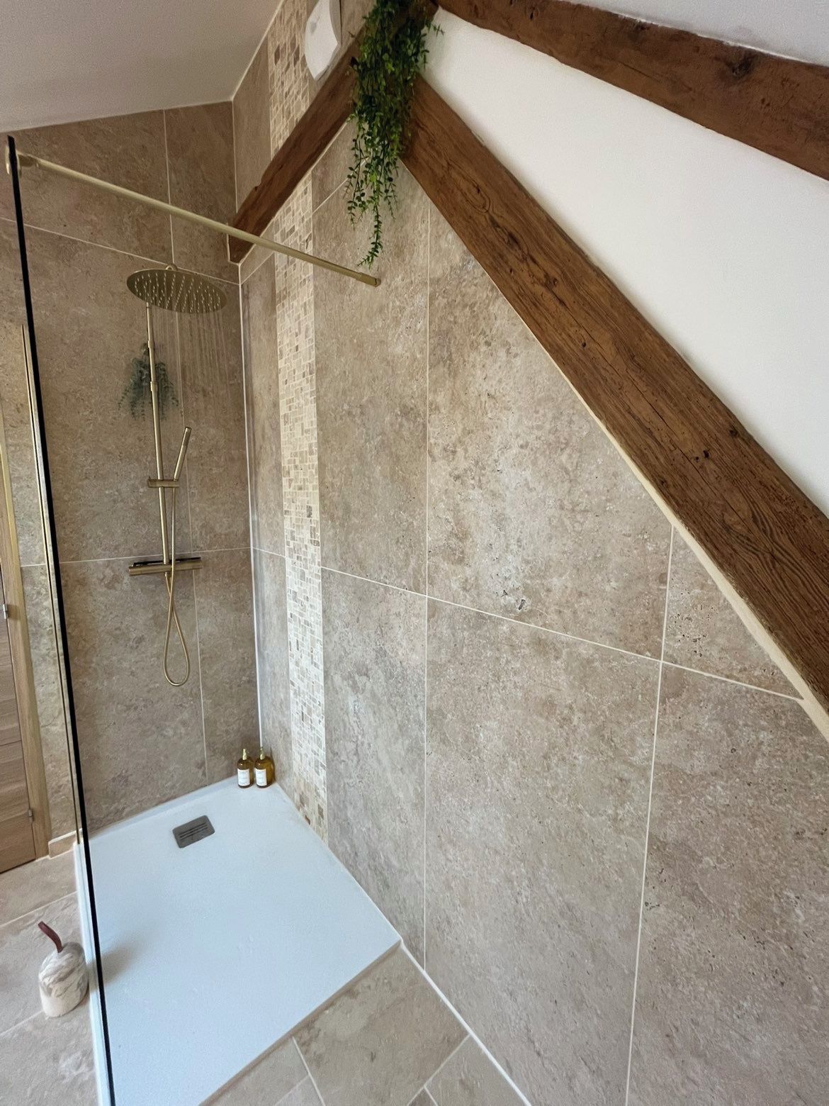Een moderne badkamer met een glazen douchecabine, een witte badkuip en een houten balk in het plafond.