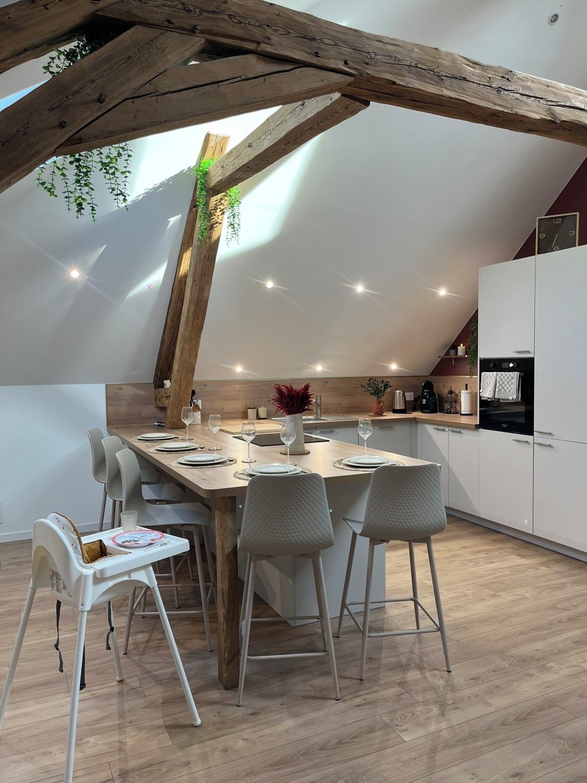 A modern kitchen with a wooden ceiling, a dining table set for four, and a child’s high chair.