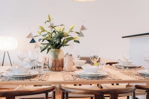Een eettafel gedekt met witte borden, kommen en glazen, omringd door houten stoelen.