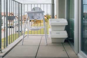 Een balkon met een witte kinderstoel en twee witte inzamelbakken voor recycling.