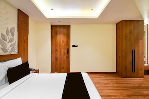 A bedroom with a bed, a wooden wardrobe, a nightstand with a phone, and a ceiling light. - Classic Palette Alamin International (Kolkata)