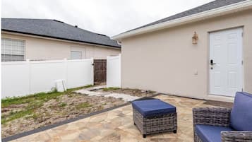 Un patio con piso de piedra, un sofá de mimbre y un pequeño reposapiés.