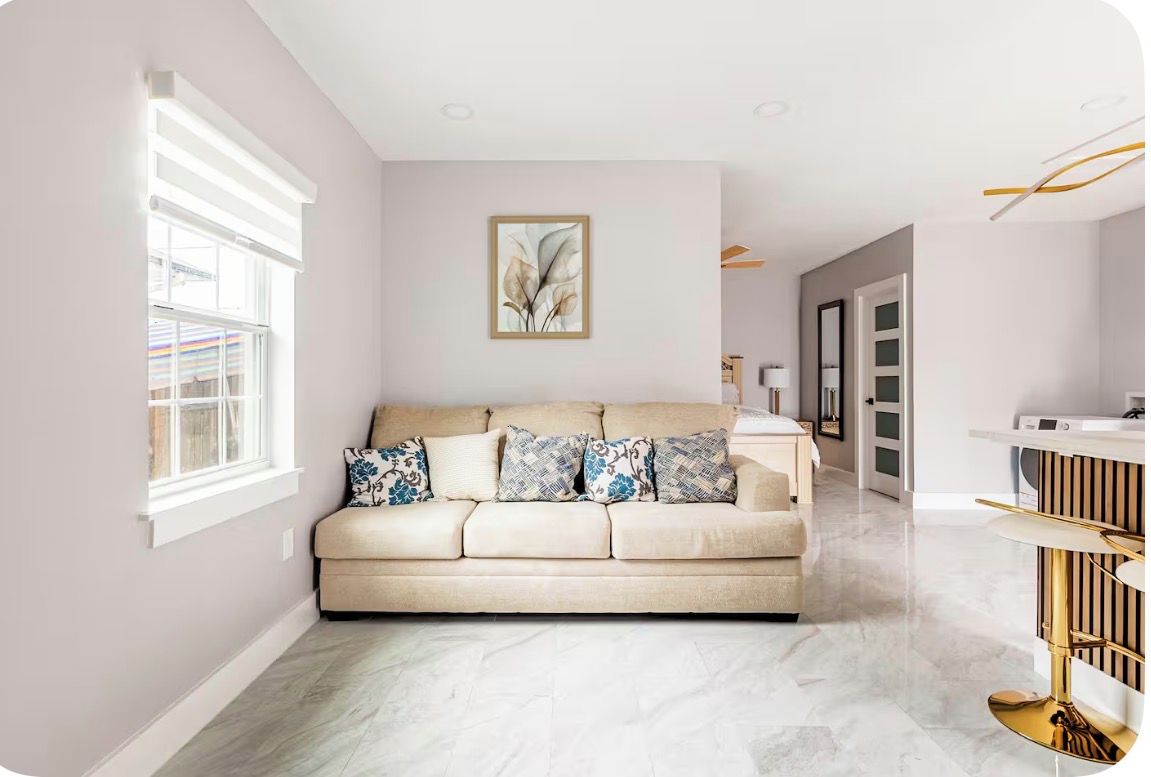 A modern living room with a beige sofa, patterned cushions, a framed abstract artwork, and a marble floor.