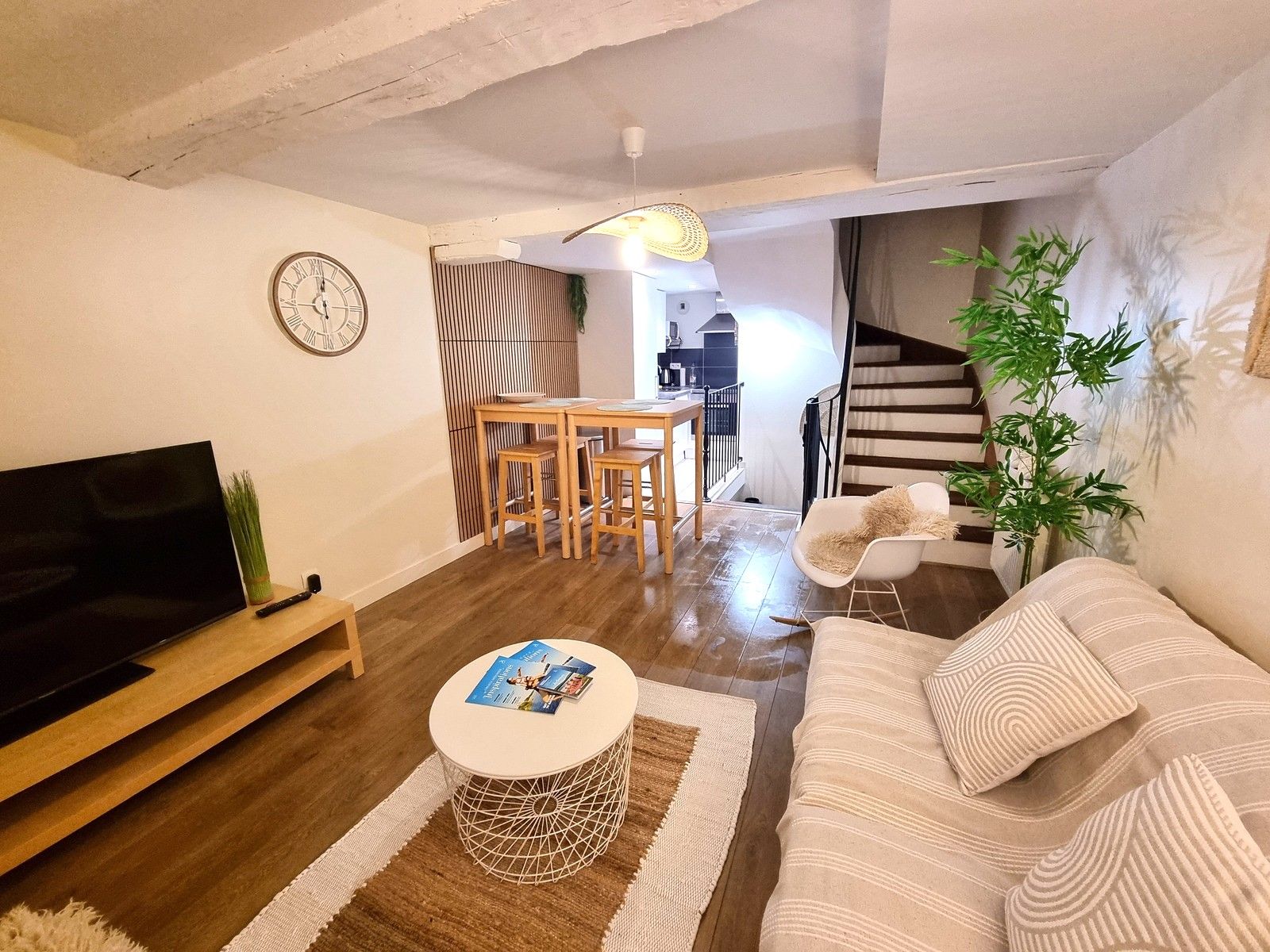Ein gemütliches Wohnzimmer mit Fernseher, Holzmöbeln, einem Essbereich und einer Treppe zu einem weiteren Raum.