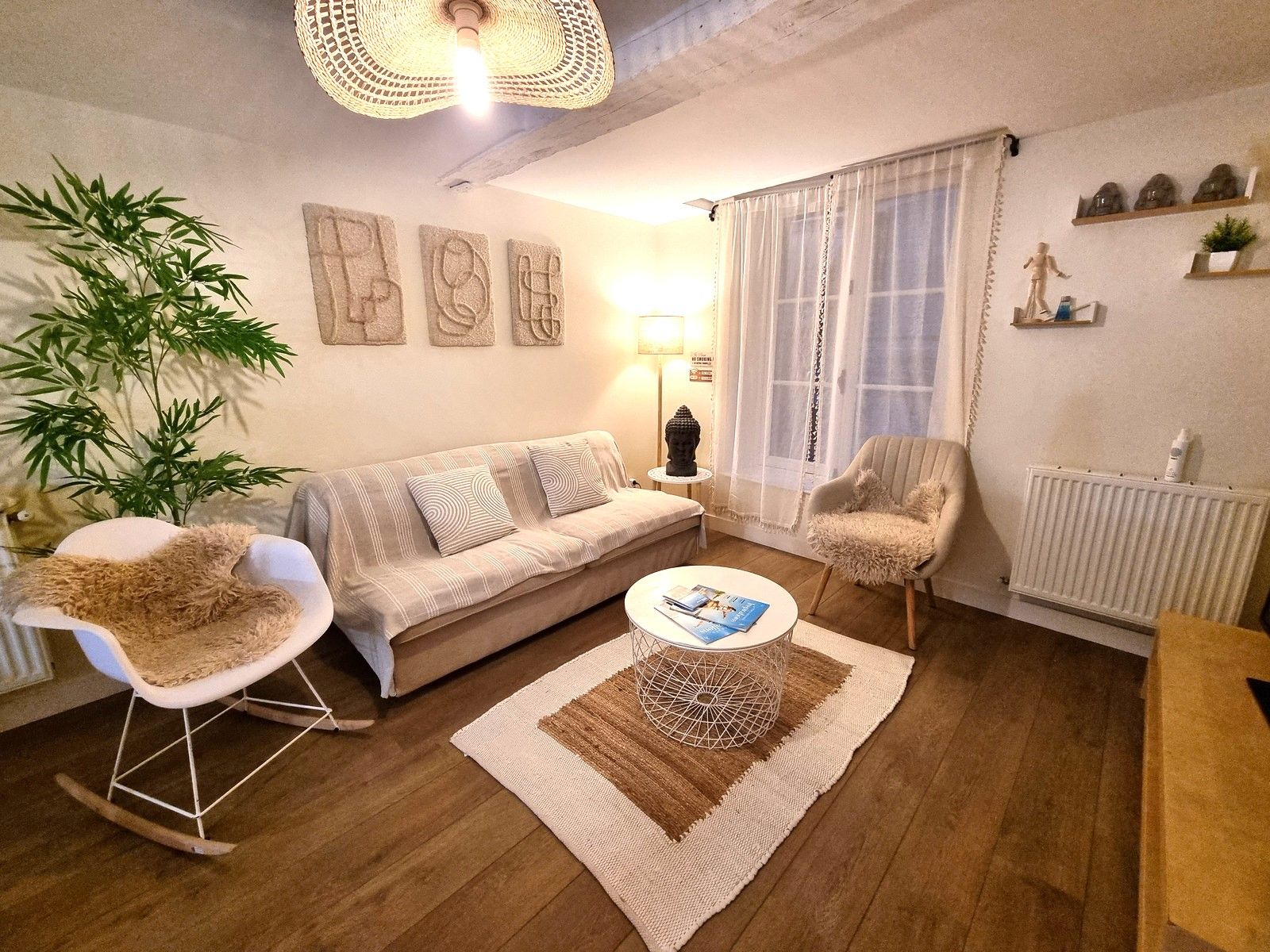 En hyggelig stue med en sofa, to lænestole, et sofabord, en lampe og en stor plante.