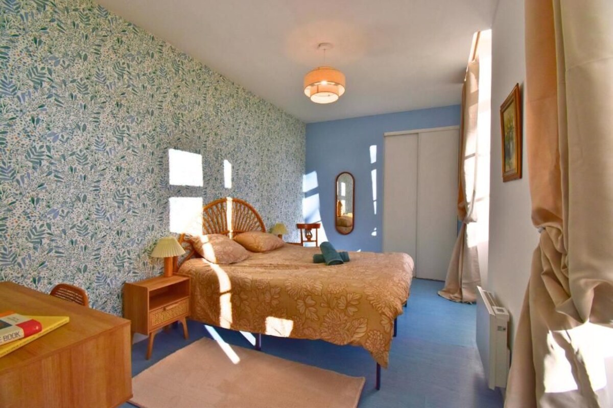 Ein Schlafzimmer mit Bett, Nachttisch, Lampe und einer Wand mit Muster.