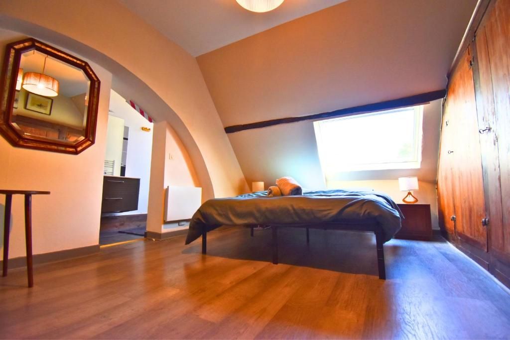 A bedroom with a bed, a wooden wardrobe, a mirror, and a window.