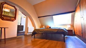A bedroom with a bed, a wooden wardrobe, a mirror, and a window.