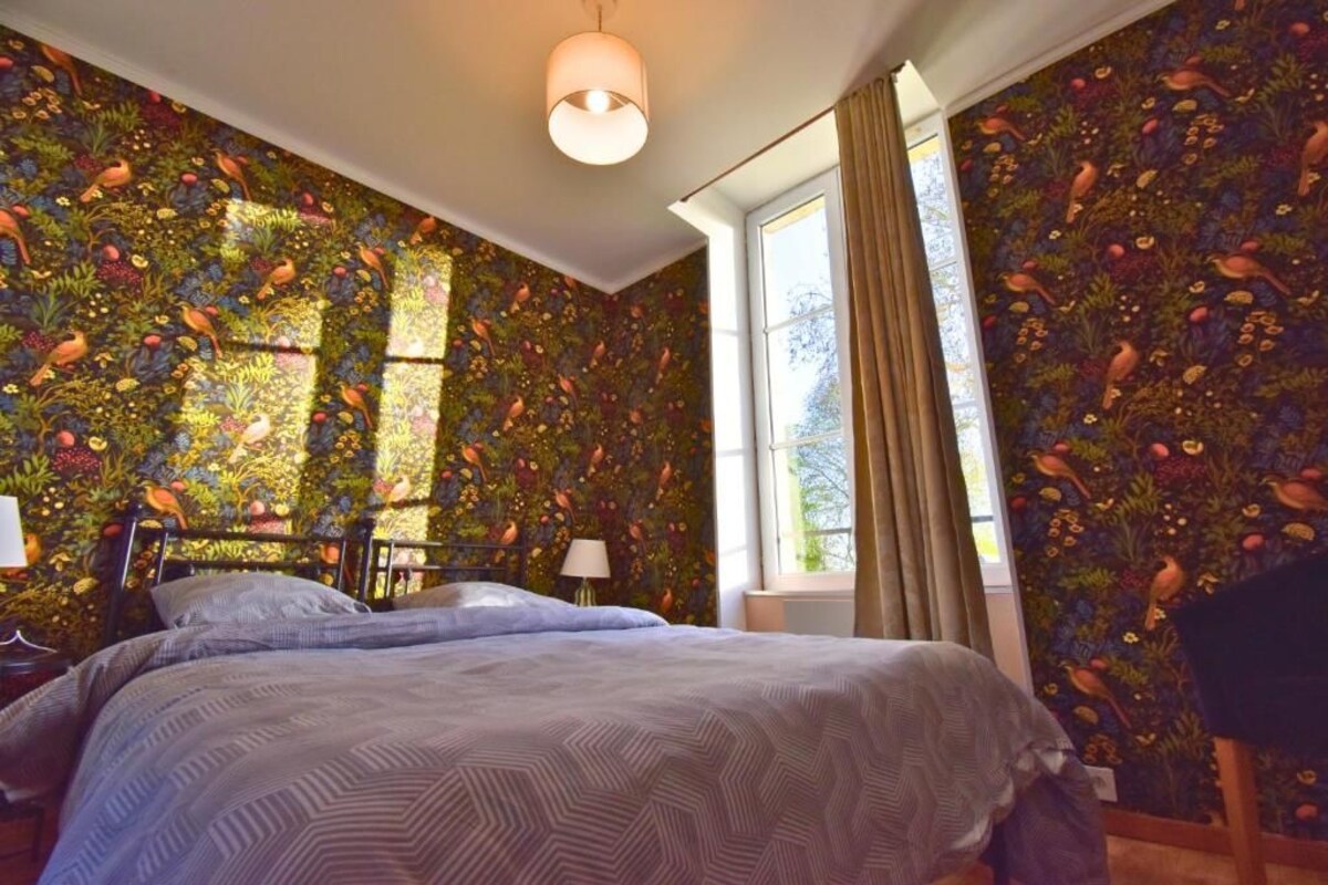 Ein Zimmer mit einem Bett, einem Fenster und einer Wand mit Vogelmuster.