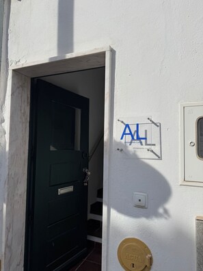 Een donkere deur met een sleutelgat en een messing sluitplaat, een witte muur met een blauw bord, en een klein raam met CE-markering.