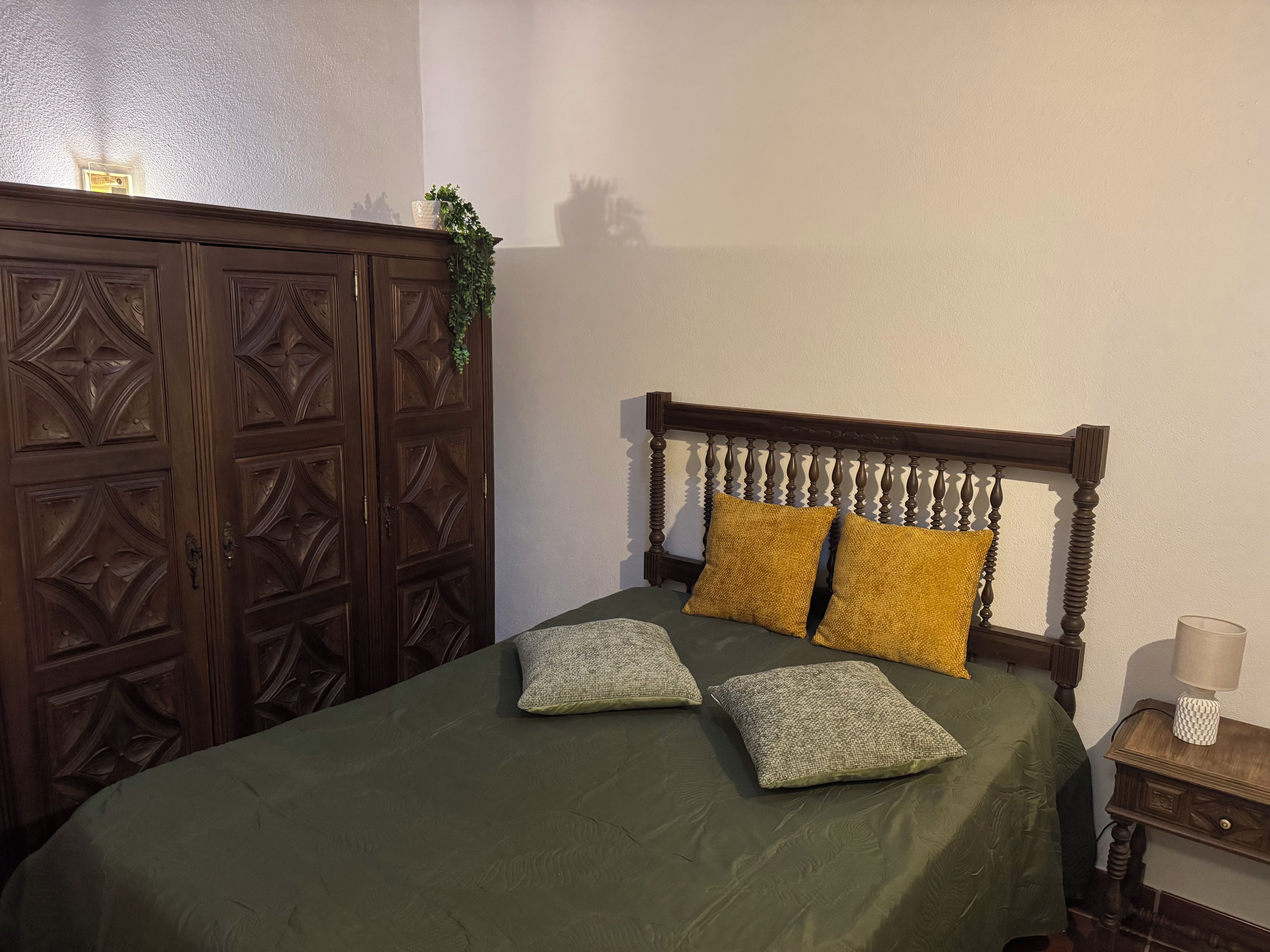 Una habitación con una cama, un armario de madera y una mesita de noche con una lámpara.