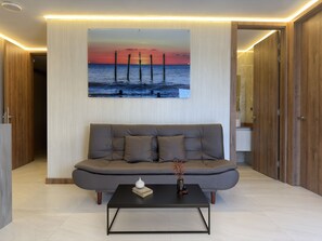 Een moderne woonkamer met een grijze bank, een zwarte salontafel en een schilderij van een zonsondergang boven water.