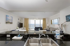 Habitación de hotel con cocina, sofá, mesa de comedor y vista al mar.