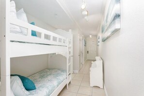 Habitación con literas, un cabecero blanco, un escritorio pequeño blanco y una puerta al fondo.