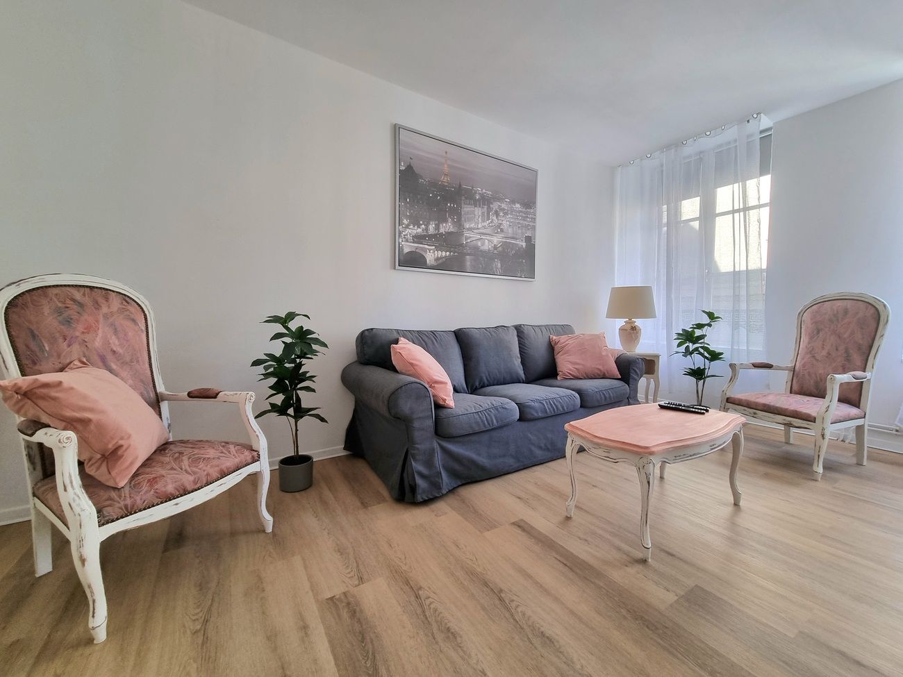 Een woonkamer met een grijze bank, twee fauteuils, een salontafel en een schilderij aan de muur.