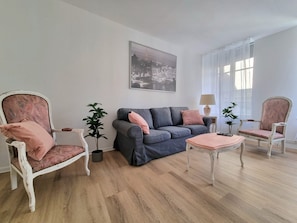 Een woonkamer met een grijze bank, twee fauteuils, een salontafel en een schilderij aan de muur.