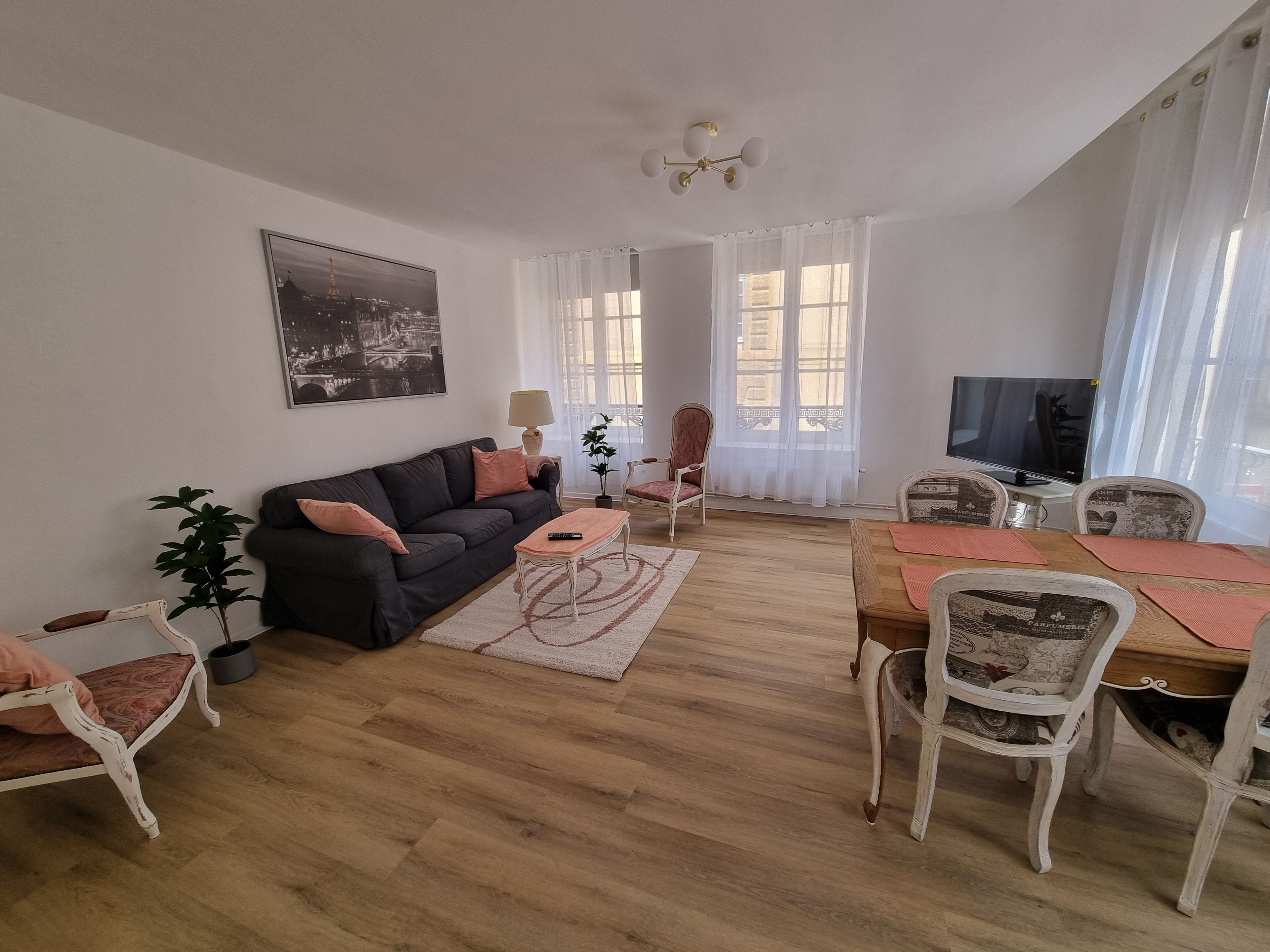 Ein Wohnzimmer mit einer Couch, einem Couchtisch, einem Esstisch mit Stühlen, einem Fernseher und einem Gemälde an der Wand.