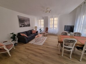 Un saló amb un sofà, una taula de centre, una taula de menjador amb caires, una televisió i un quadre a la paret.