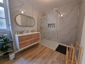 Een moderne badkamer met een douchecabine van glas, een houten wastafelmeubel en een wand met een marmerpatroon.