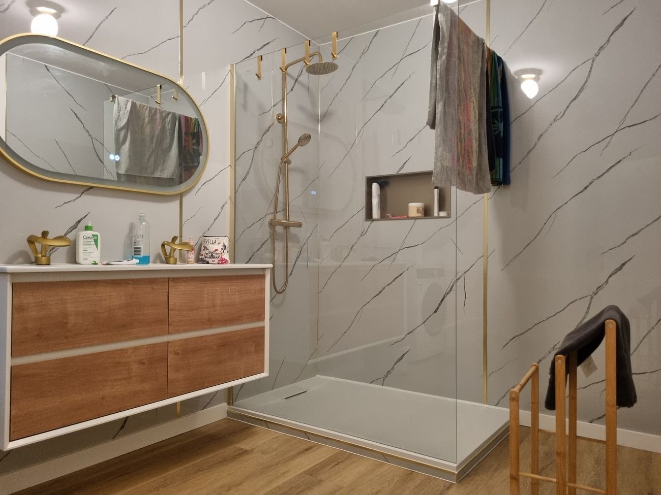 Ein modernes Badezimmer mit Marmorwand, Waschtisch aus Holz, Duschkabine aus Glas und einem Holzstuhl.