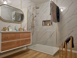 Un bany modern amb una paret de marbre, un tocador de fusta, una cabina de dutxa de vidre i una cadira de fusta.