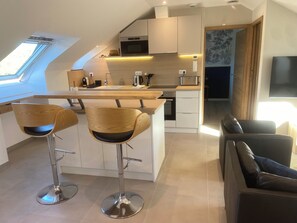 Een moderne keuken met een centraal eiland, twee barkrukken, een zithoek met een bank en een aan de muur bevestigde televisie.