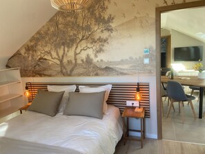 Een slaapkamer met een bed, nachtlampjes, een nachtkastje, een muurschildering en een zithoek met een tafel en stoelen.