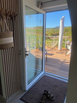 Een balkon met een houten terras, een rieten stoel en een tafel met stoelen.